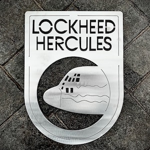 May include: A silver metal sign with the words "LOCKHEED HERCULES" in black lettering. The sign has a cutout of a Lockheed Hercules airplane.
