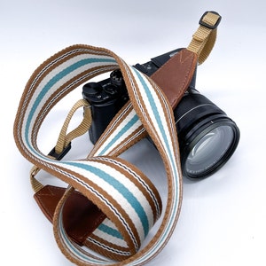 May include: A brown and white striped camera strap with a brown leather section and a black camera attached.
