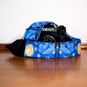 Könnte beinhalten: Ein blaues und gelbes Kameraband mit einem Sternenhimmel-Design. Das Band ist um eine schwarze Kamera mit dem aufgedruckten Wort "ZENIT" gewickelt.