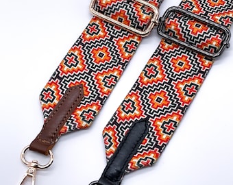 May include: Two adjustable bag straps featuring a geometric pattern in orange, black, and white. One strap has rose gold hardware with brown leather tabs, while the other has gunmetal hardware with black leather tabs and lobster claw clasps.