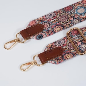 May include: A replacement bag strap featuring a colourful, intricate floral mandala pattern in shades of pink, blue, and cream. The strap includes brown leather tabs, gold-toned metal swivel lobster clasps, and a gold-toned adjustable metal slider.
