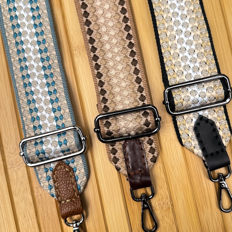 May include: Three adjustable bag straps featuring woven geometric patterns. The left strap is blue and white with brown faux leather ends. The center strap is tan and brown with dark brown leather ends. The right strap is gold and black with black leather ends.