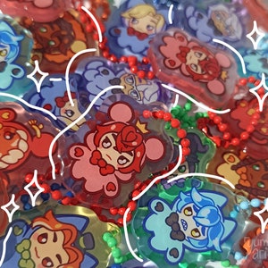 Può includere: Una collezione di portachiavi colorati con personaggi dei cartoni animati. I portachiavi sono realizzati in plastica trasparente con un effetto 3D. I personaggi sono di diversi colori e hanno espressioni diverse. I portachiavi sono attaccati a catene di perline rosse, bianche e verdi.