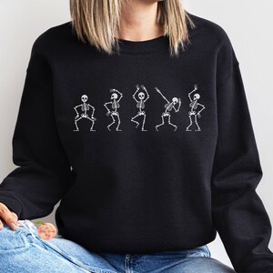 May include: Black sweatshirt with a white graphic of five skeletons dancing.