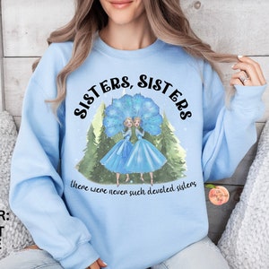 May include: Light blue sweatshirt with a graphic of two sisters wearing blue dresses and large blue feathered hats. The text reads "Sisters, Sisters, there were never such devoted sisters."