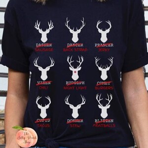 May include: Black t-shirt featuring a white reindeer graphic and the text "Dasher Sausage", "Dancer Back Strap", "Prancer Jerky", "Vixen Chili", "Rudolph Night Light", "Comet Burgers", "Cupid Tacos", "Donner Stew", and "Blitzen Meatballs".