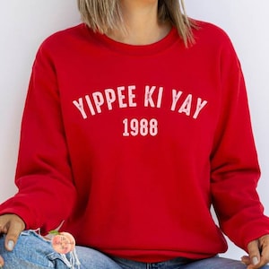 May include: Red sweatshirt with white text that reads "Yippee Ki Yay 1988".