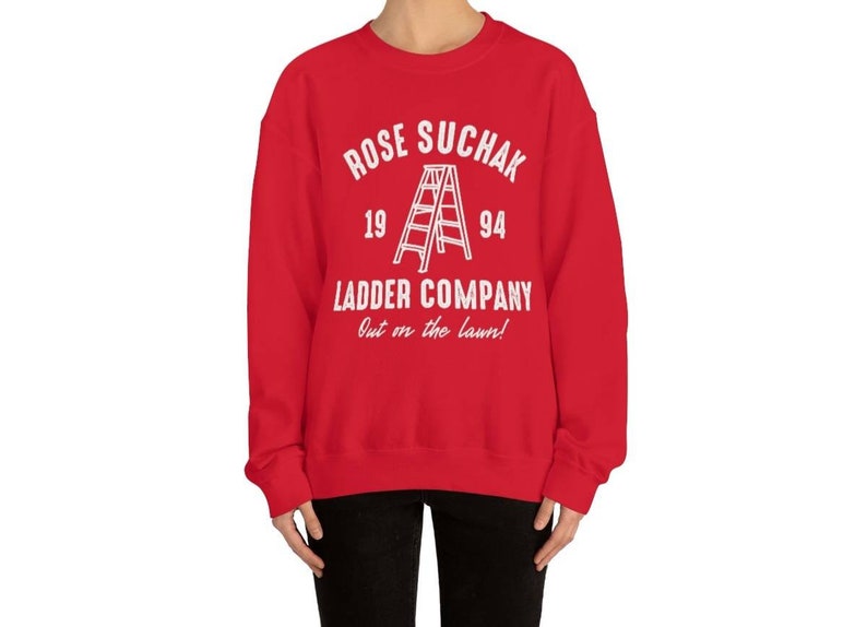K&ouml;nnte beinhalten: Roter Pullover mit wei&szlig;em Text, der "Rose Suchak Ladder Company Out on the lawn!" lautet, mit einer Leitergrafik und den Zahlen 19 und 94.