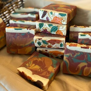 May include: A collection of handmade soap bars with an autumnal theme. The bars are swirled with shades of brown, orange, green, and white, and feature a decorative design of leaves and flowers.
