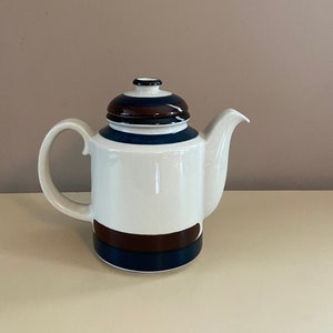 May include: A white ceramic teapot with a brown and blue striped design. The teapot has a lid and a spout.