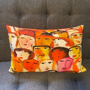 Puede incluir: Una almohada de tiro colorida con un patrón de caras abstractas en tonos de naranja, amarillo, rojo y rosa.