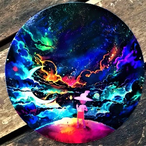 May include: A colorful painting on a round canvas depicting a night sky with a crescent moon, stars, and clouds. A small figure in a pink hat and red shorts stands on a hill in the foreground, looking up at the sky.