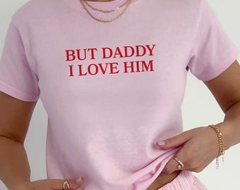 May include: A pink t-shirt with the text "BUT DADDY I LOVE HIM" in red lettering. The t-shirt is paired with matching pink shorts.