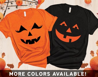 Puede incluir: Dos camisetas de Halloween. Una es naranja con una cara de calabaza, la otra es negra con una cara de calabaza. La camiseta naranja tiene pestañas. El texto "MORE COLORS AVAILABLE!" está en la parte inferior.