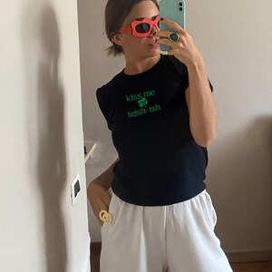 May include: A black t-shirt with the text "kiss me I'm irish-ish" and a green shamrock graphic. The person is wearing red heart-shaped sunglasses and a gold ring.