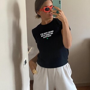 May include: A black t-shirt with the text "I'm not Irish but kiss me anyway" in white with a green heart. The person is wearing red sunglasses and a gold ring.