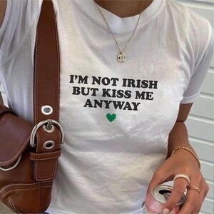 May include: White t-shirt with black text that reads "I'm not Irish but kiss me anyway" and a green heart.