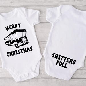 May include: Two white baby onesies. One has a black graphic of a camper van with the words "MERRY CHRISTMAS" above and below. The other onesie has the words "SHITTERS FULL" in black.