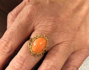 May include: A gold ring with an oval shaped coral stone set in a detailed gold filigree design.