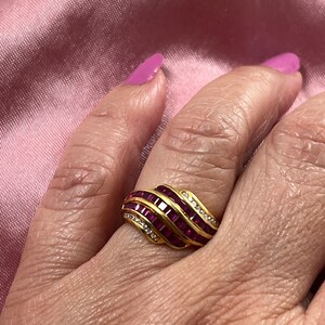 May include: A gold ring with a wavy design featuring multiple rows of ruby red and clear stones.