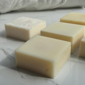 May include: Four bars of white soap on a white marble surface. The soap bars are rectangular and have a smooth, glossy finish.