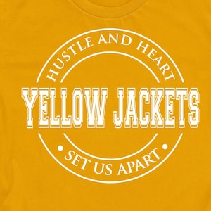 May include: Mustard yellow t-shirt with rolled-up sleeves. The shirt features a white circular design with the words "HUSTLE AND HEART" at the top, "YELLOW JACKETS" in the center, and "SET US APART" at the bottom. The Etsy shop URL is at the bottom.