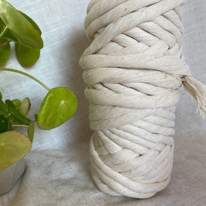 May include: A close-up of a large spool of thick, off-white cotton rope. The rope is tightly wound and has a slightly textured surface.