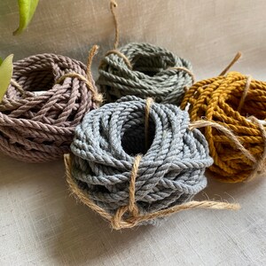 May include: Four spools of natural cotton rope in different colors: gray, brown, mustard yellow, and a lighter gray. The rope is twisted and bundled together.