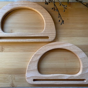 Op de afbeelding: Twee houten handvatten met een afgeronde bovenkant en een platte onderkant. De handvatten zijn gemaakt van lichtbruin hout en hebben een gladde afwerking.