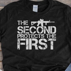 May include: Black t-shirt with a white graphic print of a rifle and the text "THE SECOND PROTECTS THE FIRST".