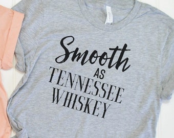 Può includere: Due magliette, una color pesca e una grigio atletico, con la scritta "Smooth as Tennessee Whiskey" in corsivo nero. La maglietta color pesca è etichettata "Peach" e la maglietta grigia è etichettata "Athletic Heather".