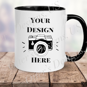 May include: White ceramic mug with a black rim and handle. The mug has a black and white illustration of a camera with the text "YOUR DESIGN HERE".