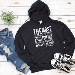 Puede incluir: Sudadera con capucha negra con un estampado gr&aacute;fico blanco que dice "THE MOST TERRIFYING WORDS IN THE ENGLISH ARE: I'M FROM THE GOVERNMENT AND I'M HERE TO HELP. -Ronald Reagan"