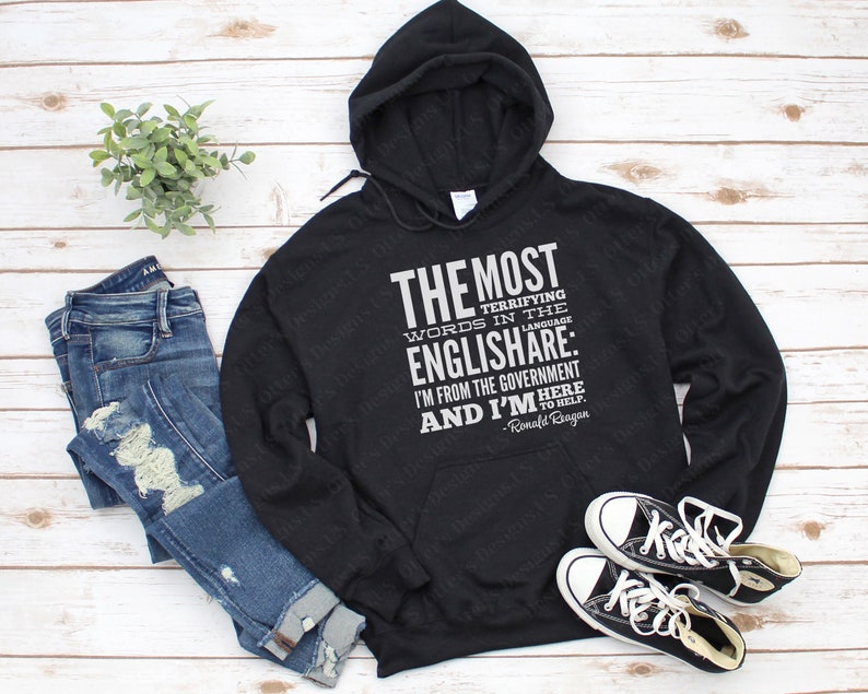 Puede incluir: Sudadera con capucha negra con un estampado gr&aacute;fico blanco que dice "THE MOST TERRIFYING WORDS IN THE ENGLISH ARE: I'M FROM THE GOVERNMENT AND I'M HERE TO HELP. -Ronald Reagan"
