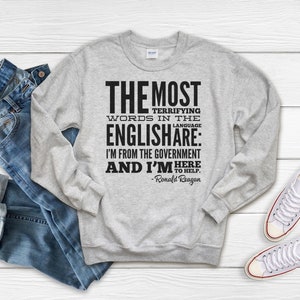 Puede incluir: Una sudadera gris con una impresi&oacute;n negra que dice "THE MOST TERRIFYING WORDS IN THE ENGLISHARE: I'M FROM THE GOVERNMENT AND I'M HERE TO HELP. -Ronald Reagan"