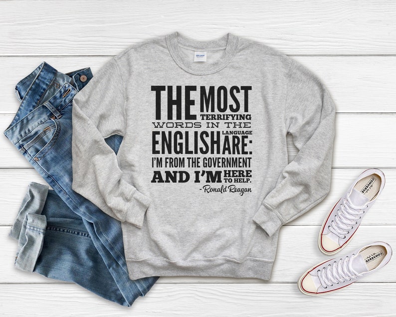 Puede incluir: Una sudadera gris con una impresi&oacute;n negra que dice "THE MOST TERRIFYING WORDS IN THE ENGLISHARE: I'M FROM THE GOVERNMENT AND I'M HERE TO HELP. -Ronald Reagan"