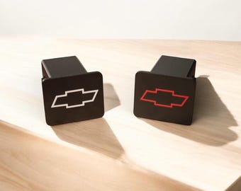 Pode incluir: Duas tampas de engate de reboque de plástico preto com um logotipo Chevrolet. Uma tampa tem um logotipo branco e a outra tem um logotipo vermelho.