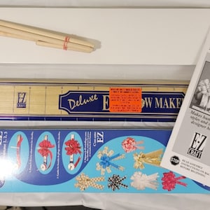 May include: A Deluxe E-Z Bowmaker kit with instructions, a wooden ruler, wooden dowels, and a blue and white box with images of bows.