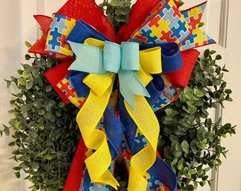 May include: A green wreath with a large bow made of red, blue, and yellow ribbon. The ribbon is patterned with puzzle pieces.
