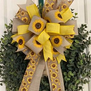 May include: A sunflower wreath with a large bow made of yellow and brown ribbon with a sunflower print. The bow is tied with a yellow ribbon.