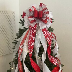 May include: A Christmas tree decorated with red and white ribbon with the words "Ho Ho Ho" printed on it. The tree is also decorated with white snowflake ornaments and white lights.