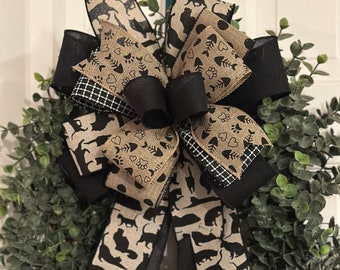 May include: A black and brown burlap wreath with a large bow featuring a black and white cat print. The bow is tied with black ribbon and has a black and white checkered pattern in the center.