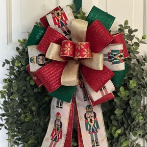 May include: A Christmas wreath with a red, gold, and green bow. The bow is decorated with nutcracker figures. The wreath is made of green eucalyptus leaves.
