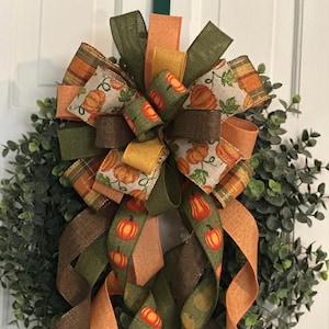 May include: A green, brown, and orange fall wreath with a large bow and pumpkin patterned ribbon.