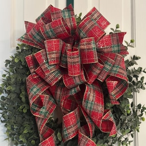 May include: A red and green plaid Christmas wreath with a large, glittery bow. The bow is made of red and green plaid ribbon with gold accents.