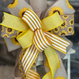 K&ouml;nnte beinhalten: Eine gelbe und wei&szlig;e gestreifte Schleife mit einem Burlap-Band mit Sonnenblumenmuster. Die Schleife ist um eine Laterne gebunden.