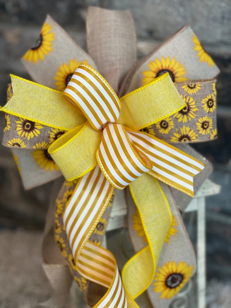 K&ouml;nnte beinhalten: Eine gelbe und wei&szlig;e gestreifte Schleife mit einem Burlap-Band mit Sonnenblumenmuster. Die Schleife ist um eine Laterne gebunden.