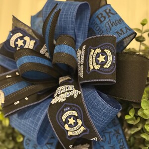 May include: Blue and black ribbon with a police officer badge design. The ribbon has the text "Protect and Serve" and "Thank you Makers".