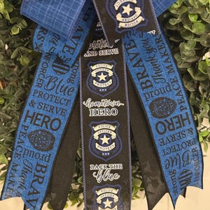 May include: Blue and black ribbon wreath with the words "Protect and Serve", "Hometown Hero", "Back the Blue", and "Brave" printed on them. The ribbons also feature a police officer badge with a star.