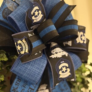 May include: A blue and black wreath with a police officer theme. The wreath is decorated with blue and black ribbon, and features a police badge with the words "Protect and Serve" and "Police Officer".